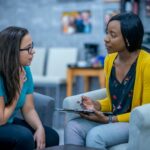Female counsellor and client sit in arm chairs next to each other, enaged in conversation