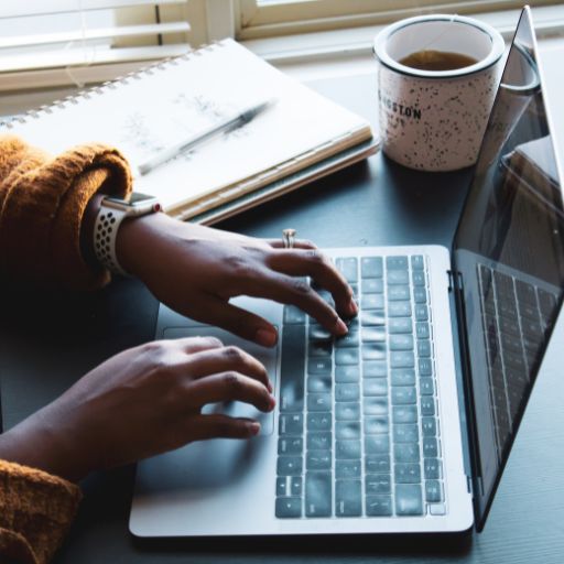 A laptop tits on a desk with hands typing on it