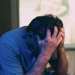 A man in a blue shirt holds his his head in his hands