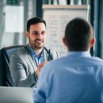 male psychologist at a desk, talking to male client in foreground
