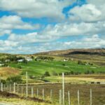 a rural landscape with green and brown pastures and rolling hills on the horizon